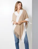 Poncho de tejido soft, color beige y blanco, con diseño cruzado en el frente y cuello en V. Presenta bordes y flecos en color blanco.