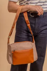 Bandolera de diseño moderno, color beige rosado, con correa regulable y bolsillo frontal con cierre.