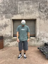 Remera verde oliva de algodón con estampado en la espalda que incluye un símbolo de reciclaje, el logo de la marca Xtreme Wear, la frase 'Breaking Rules' y un texto con tipografía pequeña.