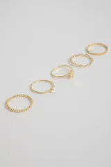 Set de cinco anillos dorados con diferentes diseños: uno liso, uno con pequeñas esferas, uno con un dije de moño, uno con un dije de strass y uno con textura trenzada.