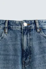 Jeans de denim de algodón, color negro lavado, con tiro medio, corte ajustado en cadera y muslos, y pierna que se estrecha hacia el tobillo. Presenta cinco bolsillos y cierre frontal con cremallera y botón.