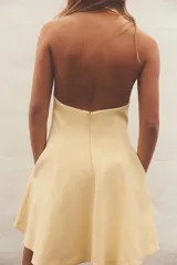 Vestido corto amarillo con cuello halter y espalda descubierta. Falda con vuelo y cierre trasero con cremallera oculta y botones ocultos en el cuello.