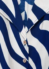 Camisa de viscosa blanca con estampado abstracto en azul, corte crop, cuello camisero, mangas cortas y nudo decorativo en el frente.