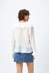 Blusa blanca de gasa con escote en V y volados en el cuello y las mangas largas. Se ata con lazos finos al frente.