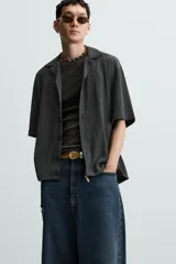Camisa de manga corta con cuello bowling y calce relajado. Presenta un tejido con textura estructurada y efecto lavado, con cierre frontal de botones al tono.