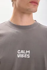 Remera gris con estampa en la espalda que dice "Calm Vibes" con una flor en el medio. Corte amplio y recto, con proporciones cuadradas.