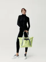 Bolso tipo tote de poliéster color verde oliva con asas de cinta negra. Tiene cierre superior y seis bolsillos externos, uno con ajuste elástico y otro con cremallera.