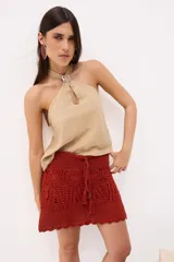 Top de lino color beige con cuello halter cruzado y detalle de hebilla metálica cuadrada en el frente. Presenta una pequeña abertura central tipo gota y un diseño fluido sin mangas.