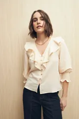 Camisa blanca a rayas verticales, con escote en V, mangas 3/4 con puños elastizados y volados.