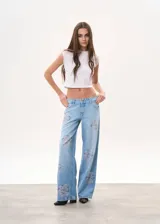Pantalón de jean celeste de tiro bajo, corte wide leg y apliques de strass con forma de rosa en ambas piernas.