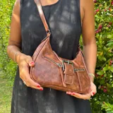 Cartera marrón de eco cuero con correa de hombro ajustable y cierre con hebilla metálica.
