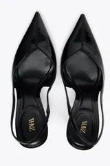 Zapato destalonado acharolado color negro, con tacón fino y punta. Tiene una tira trasera con elástico.