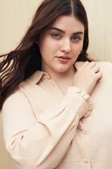 Camisa blanca de manga larga con textura sutil y caída fluida. Presenta cuello clásico, botones forrados a tono y puños con terminación fruncida.