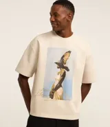 Remera overboxy color crema con estampa frontal de una mujer con un pájaro en la cabeza y lettering bordado.