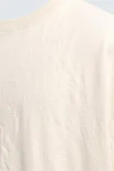 Camiseta color crema de corte holgado, confeccionada en tejido con textura arrugada y cuello redondo.