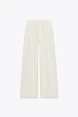 Pantalón palazzo color crudo, de tiro alto, confeccionado en lyocell. Presenta bolsillos laterales ocultos, detalle de pliegues en el delantero y cierre frontal con cremallera y botones.