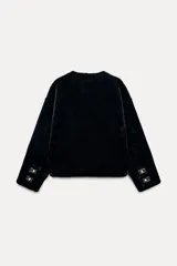 Chaqueta corta de cuello redondo y manga larga en tejido de pelo sintético color negro. Cierre frontal con botones metálicos dorados y bolsillos de plastrón. Colección Zara Woman.