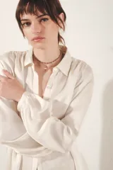 Camisa color blanco hueso de corte fluido, con cuello camisero, mangas largas abullonadas con puño abotonado y detalle de frunces.