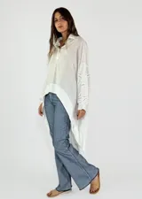 Blusa blanca de mangas largas con detalles de encaje en las mangas y cuello polo con cierre parcial.