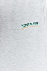 Pantalón de jogging gris claro, de tiro alto, con cintura elástica ajustable con cordones, bolsillos laterales y texto estampado en el frente.