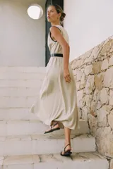 Vestido midi de lino color beige, con escote cruzado en pico y sin mangas. Presenta vivos a contraste en negro y cinturón con hebilla forrada. Cierre frontal con botones.