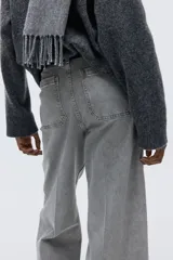 Pantalón de jean de tiro alto, color gris lavado, con pierna ancha y puños doblados. Presenta bolsillos de parche grandes en la parte delantera y bolsillos traseros.