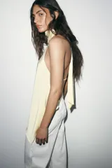 Top sin mangas color blanco, con cuello halter drapeado y bajo asimétrico con caída.