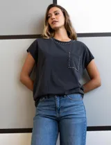 Remera gris de algodón con cuello redondo, mangas cortas y bolsillo en el pecho. Apliques de tachas plateadas en cuello, hombros y bolsillo.