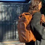 Mochila de eco-cuero color marrón, con múltiples bolsillos frontales y laterales, y asa superior.