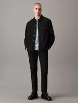 Pantalón chino negro de corte tapered, confeccionado en sarga de algodón elástica. Cuenta con cierre de botón y cremallera, bolsillos con ranura y bolsillos traseros de ojal.