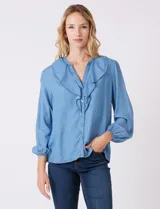 Blusa de lyocell color azul claro, con escote en V y volados en el cuello y la parte frontal. Tiene mangas largas con puños elásticos y cierre de botones en la parte delantera.