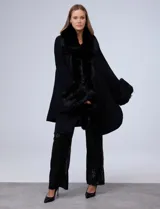 Ruana tejida negra con cuello, borde frontal y puños de piel sintética. Presenta un cierre frontal con botón tipo trenca.