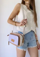 Bandolera rectangular de cuero color lila, con detalles en marrón y blanco. Tiene correa larga regulable, bolsillo frontal con cierre y etiqueta de cuero con logo de la marca.