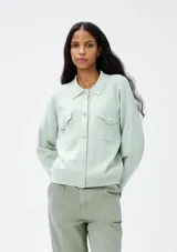 Chaqueta color verde agua con cuello camisero, cierre frontal con botones, dos bolsillos de parche con solapa en el pecho y mangas largas.
