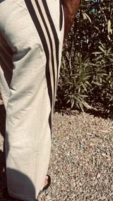 Pantalón de jogging color gris claro, corte ancho, con cordón ajustable en la cintura y tres rayas negras verticales en los laterales.