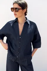 Camisa de denim azul con cuello de solapa, escote en pico, cierre frontal con botones y mangas anchas hasta el codo.