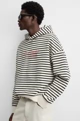 Sudadera con capucha a rayas horizontales blancas y negras, corte boxy fit, mangas largas y texto bordado en color rosa en el pecho.