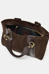Bolso de mano tipo mini shopper en color marrón oscuro, confeccionado en material tipo gamuza o nobuk, con detalles de cuero liso en las asas y tiras laterales. Presenta herrajes metálicos dorados con forma de doble 'C' o anillo.