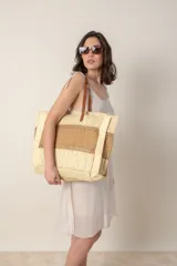 Bolso tipo shopper de rafia color beige con franja horizontal color camel. Tiene asas de cuero color marrón para llevar al hombro y cierre superior.
