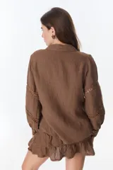 Camisa celeste de lino con cuello clásico, abotonada al frente y mangas largas con detalle de puntilla en los hombros.
