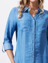 Camisa celeste de lyocell, con cuello a la base, escote en V y abertura central con botones. Tiene bolsillos aplicados en la parte delantera y mangas 3/4 regulables con presilla y botón.