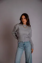 Buzo gris de punto con cuello redondo, mangas largas abullonadas y cierre frontal asimétrico.
