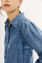 Camisa celeste de tencel con calce recto, manga larga amplia con frunces en los hombros y cuello camisero. Mangas terminadas en puño con botón y ojal. Cartera delantera con botones metálicos con el logo de la marca.