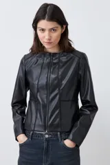Chaqueta corta de cuero sintético color negro, con cuello redondo y cierre frontal. Presenta detalle de pasamanería en hombros y cuello.