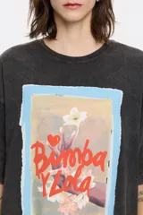 Camiseta color crema de algodón con estampado de un cuadro con borde celeste, con una mano sosteniendo una flor y el texto "Bimba y Lola".