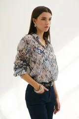 Camisa celeste con estampado abstracto en tonos marrones y azules, de corte clásico, cuello camisero y mangas largas con puños abotonados.
