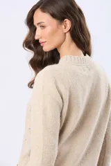 Buzo tejido de abrigo color beige, con cuello redondo y mangas largas. Presenta un delicado diseño bordado en el frente con pequeños motivos en tonos pastel.