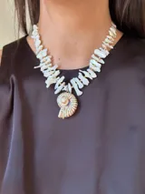 Collar corto con cuentas irregulares de nácar color blanco y dije de caracol con detalles dorados. Cierre con gancho y cadena de acero quirúrgico para regular el largo.