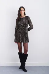 Vestido corto negro con estampado abstracto dorado, escote redondo, mangas largas con elástico en los puños, detalle de nudo drapeado en la cintura y escote en V pronunciado en la espalda.
