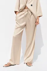 Pantalón de tiro alto color beige con cintura elástica ajustable con cordones, bolsillos delanteros y pernera ancha.